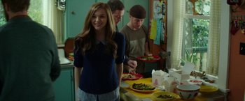 Movie still from “If I Stay” (2014), directed by R.J. Cutler – A woman standing in front of a table with plates of food on it; Medium shot, Over the shoulder angle