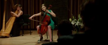 Movie still from “If I Stay” (2014), directed by R.J. Cutler – A woman in a green dress playing the cello; Wide shot, Over the shoulder angle