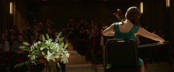 Movie still from “If I Stay” (2014), directed by R.J. Cutler – A woman in a green dress is holding a microphone; Wide shot, Over the shoulder angle
