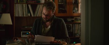 Movie still from “If I Stay” (2014), directed by R.J. Cutler – A man sitting at a table looking at papers; Medium shot, Over the shoulder angle