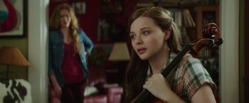Movie still from “If I Stay” (2014), directed by R.J. Cutler – A young woman holding a cello in a living room; Close Up shot, Over the shoulder angle