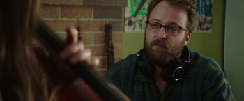 Movie still from “If I Stay” (2014), directed by R.J. Cutler – A man with a beard wearing headphones and a plaid shirt; Close Up shot, Over the shoulder angle