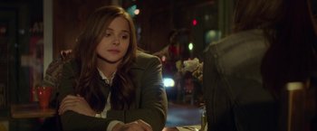 Movie still from “If I Stay” (2014), directed by R.J. Cutler – A woman sitting at a table in front of a window; Close Up shot, Over the shoulder angle