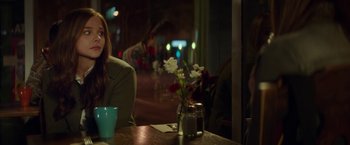 Movie still from “If I Stay” (2014), directed by R.J. Cutler – A woman sitting at a table with a vase of flowers in front of her; Medium shot, Over the shoulder angle