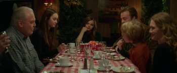 Movie still from “If I Stay” (2014), directed by R.J. Cutler – A group of people sitting at a table with a cake; Medium shot, Over the shoulder angle
