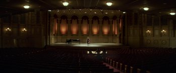 Movie still from “If I Stay” (2014), directed by R.J. Cutler – A person standing in front of a piano in a theater; Extreme Wide shot, High angle