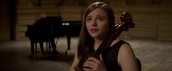 Movie still from “If I Stay” (2014), directed by R.J. Cutler – A woman holding a violin in a room; Medium shot, Over the shoulder angle