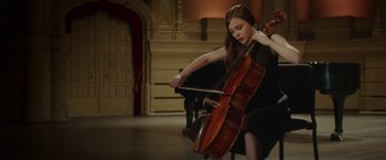 A woman in a black dress playing a cello in a room