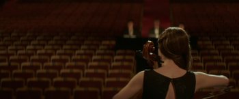 Movie still from “If I Stay” (2014), directed by R.J. Cutler – A woman in a black dress holding a violin in front of an audience; Wide shot, Over the shoulder angle
