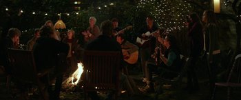 Movie still from “If I Stay” (2014), directed by R.J. Cutler – A group of people sitting around a fire with guitars; Wide shot, High angle