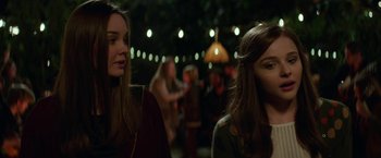 Movie still from “If I Stay” (2014), directed by R.J. Cutler – Two young women standing next to each other in front of lights; Close Up shot, Over the shoulder angle