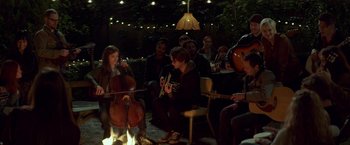 Movie still from “If I Stay” (2014), directed by R.J. Cutler – A group of people sitting around a campfire playing instruments; Wide shot, Over the shoulder angle