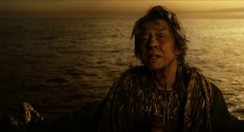 Movie still from “Immortals” (2011), directed by Tarsem Singh – An old man with a beard and a long hair is standing by the water; Close Up shot, High angle