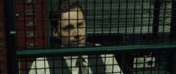 Movie still from “In Time” (2011), directed by Andrew Niccol – A man wearing a suit and tie sitting in a cage; Close Up shot, Low angle