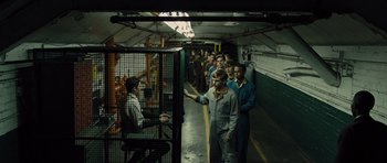 Movie still from “In Time” (2011), directed by Andrew Niccol – A group of men standing in a line in front of a cage; Wide shot, High angle