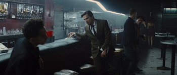 Movie still from “In Time” (2011), directed by Andrew Niccol – A man in a suit and tie standing next to a bar; Medium shot, Low angle