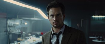 Movie still from “In Time” (2011), directed by Andrew Niccol – A man wearing a suit and tie standing in a room; Close Up shot, Over the shoulder angle