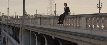 Movie still from “In Time” (2011), directed by Andrew Niccol – A man in a suit sitting on the edge of a bridge; Wide shot, High angle