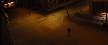 Movie still from “In Time” (2011), directed by Andrew Niccol – A person is running on the sidewalk at night; Extreme Wide shot, High angle