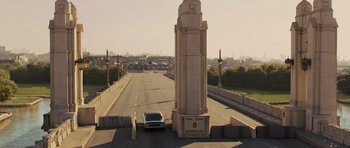 Movie still from “In Time” (2011), directed by Andrew Niccol – A car driving down a street next to a tall pillar; Extreme Wide shot, High angle