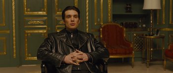 Movie still from “In Time” (2011), directed by Andrew Niccol – A man sitting in a chair wearing a black leather jacket; Medium shot, Low angle