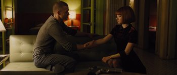 Movie still from “In Time” (2011), directed by Andrew Niccol – A man and a woman sitting on a couch holding hands; Medium shot, Over the shoulder angle