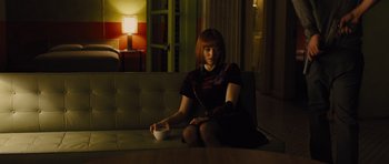 Movie still from “In Time” (2011), directed by Andrew Niccol – A woman sitting on top of a couch holding a coffee cup; Medium shot, High angle