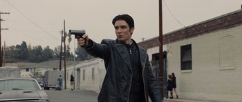 Movie still from “In Time” (2011), directed by Andrew Niccol – A man holding a gun while standing on the side of the road; Medium shot, Low angle