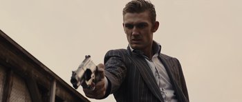 Movie still from “In Time” (2011), directed by Andrew Niccol – A man in a suit and tie holding a gun in his hand; Close Up shot, Low angle