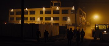 Movie still from “In Time” (2011), directed by Andrew Niccol – A group of people standing in front of a building at night; Extreme Wide shot, High angle