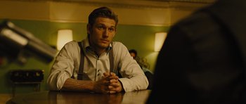 Movie still from “In Time” (2011), directed by Andrew Niccol – A man sitting at a table with his hands crossed; Medium shot, Over the shoulder angle