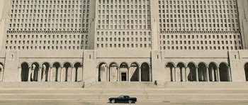 Movie still from “In Time” (2011), directed by Andrew Niccol – A car is parked in front of a large building; Extreme Wide shot, High angle