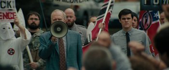 Movie still from “Imperium” (2016), directed by Daniel Ragussis – A man with a megaphone in front of a group of people; Medium shot, Over the shoulder angle