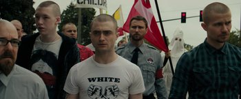 Movie still from “Imperium” (2016), directed by Daniel Ragussis – A group of people marching down a street holding flags; Medium shot, Over the shoulder angle