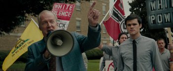 Movie still from “Imperium” (2016), directed by Daniel Ragussis – A man with a megaphone in front of a group of people; Medium shot, Over the shoulder angle