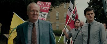 Movie still from “Imperium” (2016), directed by Daniel Ragussis – A man in a suit and tie holding a flag; Medium shot, Over the shoulder angle
