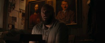 Movie still from “Imperium” (2016), directed by Daniel Ragussis – A man sitting in front of a painting of adolf hitler; Medium shot, Low angle