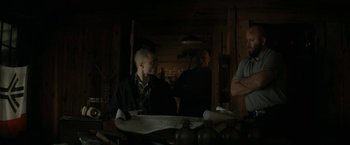 Movie still from “Imperium” (2016), directed by Daniel Ragussis – A man sitting at a table with a skateboard; Medium shot, Over the shoulder angle