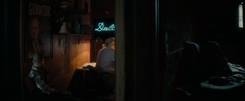 Movie still from “Imperium” (2016), directed by Daniel Ragussis – A person sitting at a table in front of a neon sign; Wide shot, Low angle