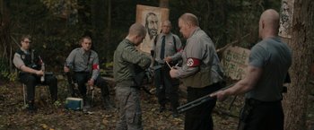 Movie still from “Imperium” (2016), directed by Daniel Ragussis – A group of men standing in front of a painting; Medium shot, Over the shoulder angle