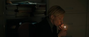 Movie still from “Imperium” (2016), directed by Daniel Ragussis – A woman sitting in a dark room with a cigarette in her mouth; Medium shot, High angle