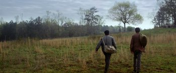 Movie still from “In Dubious Battle” (2016), directed by James Franco – A man walking through a grassy field with a bag; Wide shot, Low angle