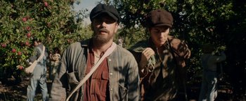 Movie still from “In Dubious Battle” (2016), directed by James Franco – A man and a woman wearing hats standing next to each other; Medium shot, Low angle