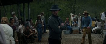 Movie still from “In Dubious Battle” (2016), directed by James Franco – A man in a hat standing in front of a group of people; Medium shot, Over the shoulder angle