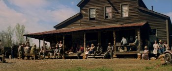 Movie still from “In Dubious Battle” (2016), directed by James Franco – A group of people sitting on the porch of a wooden house; Extreme Wide shot, High angle