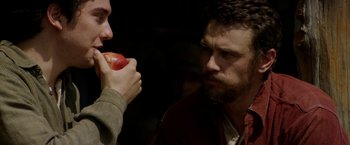 Movie still from “In Dubious Battle” (2016), directed by James Franco – A man eating an apple with another man holding it; Close Up shot, Over the shoulder angle