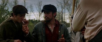 Movie still from “In Dubious Battle” (2016), directed by James Franco – A man smoking a cigarette while standing next to a tree; Medium shot, Over the shoulder angle