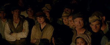 Movie still from “In Dubious Battle” (2016), directed by James Franco – A group of people sitting in a dark room wearing hats; Medium shot, High angle