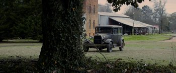 Movie still from “In Dubious Battle” (2016), directed by James Franco – An old car parked in the grass next to a building; Extreme Wide shot, High angle