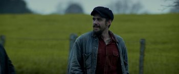 Movie still from “In Dubious Battle” (2016), directed by James Franco – A man wearing a hat and a jean jacket standing in front of a field; Medium shot, Low angle